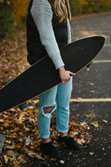 Cropped view of woman holding longboard in parking lot with leaves