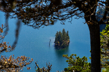 Overhead view of a tiny island in bright blue ocean framed in the foreground by tree branches -...