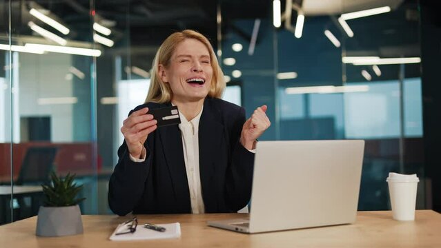 Excited businesswoman receiving email with good news on computer. Portrait of beautiful successful female entrepreneur holding credit card looking at laptop screen reading winner message in office.