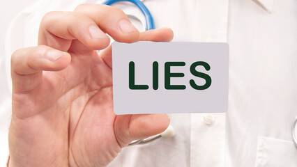 Lies word on the card in a man's hand on the background of a white shirt - obrazy, fototapety, plakaty