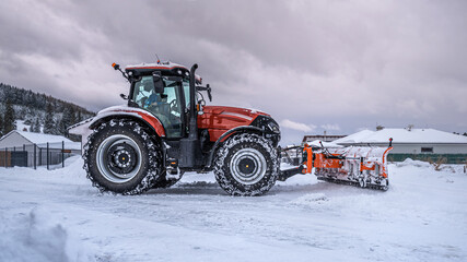 The snow plow tractor while snow clearing on the street.