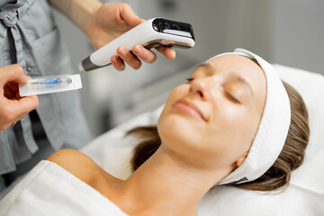 Young woman before a beauty procedure with dermapen, cosmetologist holds dermapen with needle near client's face