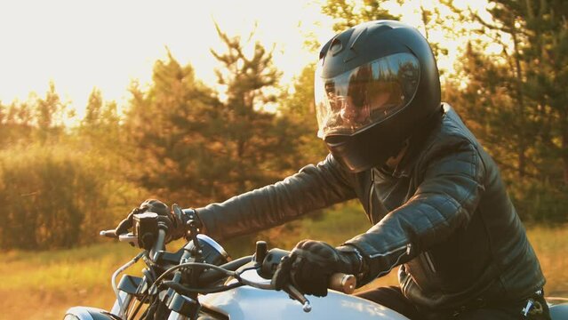 Portrait of biker in sunglasses and black helmet driving at high speed in countryside at sunset