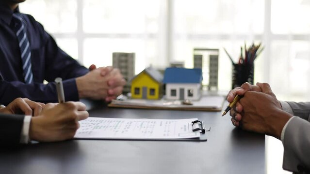Businessman is negotiating a contract for the purchase and sale of a house. Real estate agent is offering a house for sale and a businessman signs an agreement document.