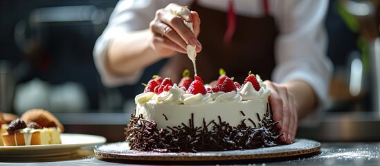 cooking and decoration of cake with cream Young woman pastry chef in the kitchen decorating red velvet cake with flowers and berries Master pastry chef completes work on a birthday cake