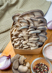 A bunch of oyster mushrooms in a craft box on a kitchen board. Fresh oyster mushrooms with red onion, peppercorns and pink salt on a kitchen board. The process of preparing mushrooms.