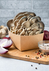 A bunch of oyster mushrooms in a craft box on a kitchen board. Fresh oyster mushrooms with red onion, peppercorns and pink salt on a kitchen board. Close.