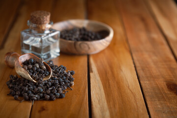 Dry organic Sheetal Chini (Piper cubeba) seeds, in a wooden scoop and bowl, along with its essential oil.