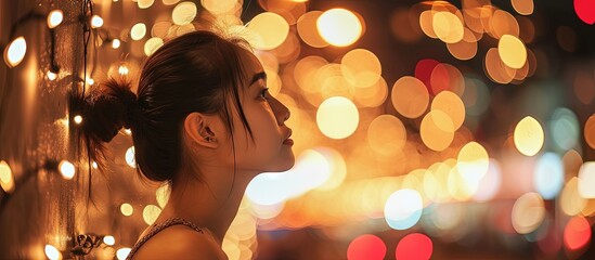 Charming young woman in casual clothes making hair ponytail and looking away while sitting against illuminated fairy lights in showroom during Christmas holidays. Creative Banner. Copyspace image