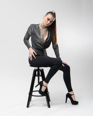A girl in high-heeled shoes and a glamorous outfit poses sitting on a bar stool