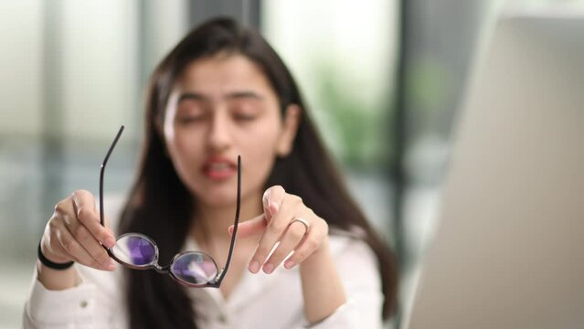 Young businesswoman expressing misunderstanding or tiredness while sitting by desk in front of laptop and looking through online data
