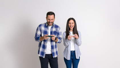 Cheerful young couple laughing and playing video games on mobile phones isolated over white background