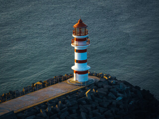 Red and white striped lighthouse on seaside in morning sunlight