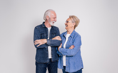 Cheerful senior couple with arms crossed looking at each other and talking against white background