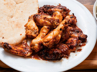 Big portion of barbeque marinated and cooked chicken wings and pitta bread on a white plate. Simple tasty food.