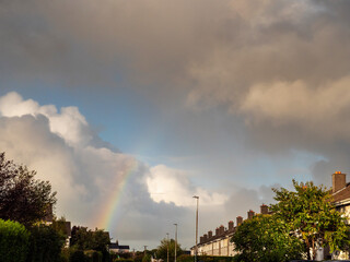 Cloudy sky with colorful rainbow over a high density living area with houses.