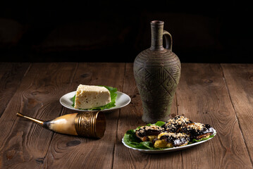 Wine in an amphora, a horn  glass, eggplant rolls, cheese and sesame seeds on a wooden table....