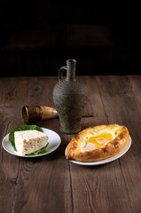 Wine in an amphora, a horn glass, cheese pie eggplant rolls, cheese and sesame seeds on a wooden table. Traditional Georgian feast