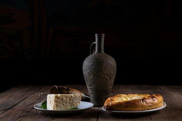 Wine in an amphora, a horn glass, cheese pie eggplant rolls, cheese and sesame seeds on a wooden...