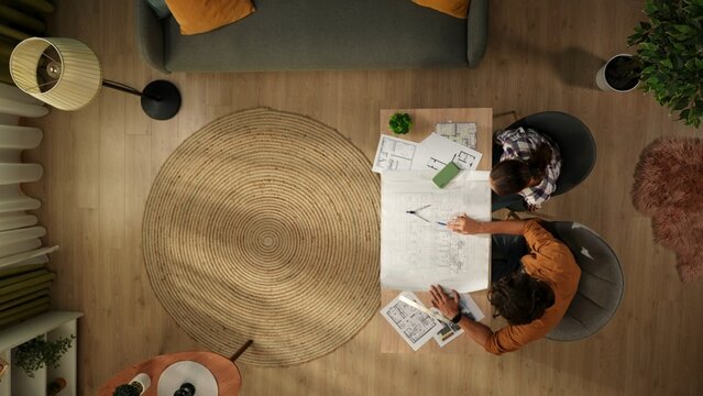 Top view capturing a woman and a man working in a home office. Young architects are looking through, comparing the blueprints of the building and discussing them.