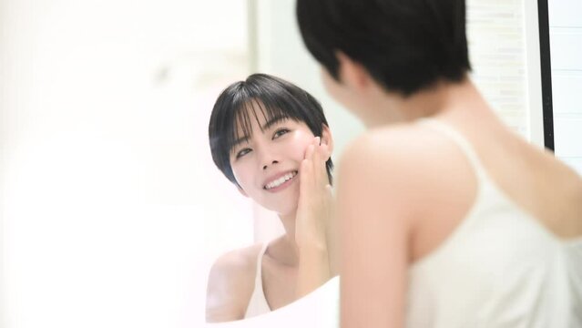 美容などのイメージで使いやすい洗面台で鏡を見る美しい女性のカメラ目線で頬を触る動画