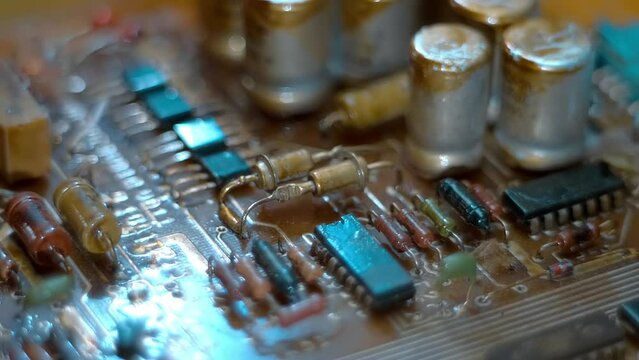 On the old board there are many parts filled with varnish to prevent short circuits - microchips, resistors, diodes, transistors and capacitors. Closeup. Macro. Shallow depth of field. Shot in motion