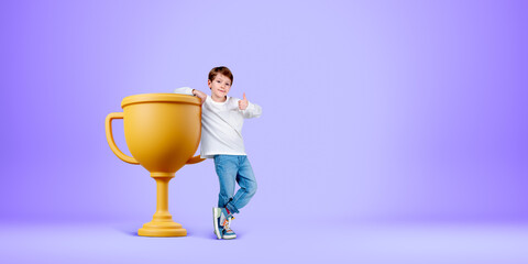 Boy with thumb up standing near gold cup on empty purple background