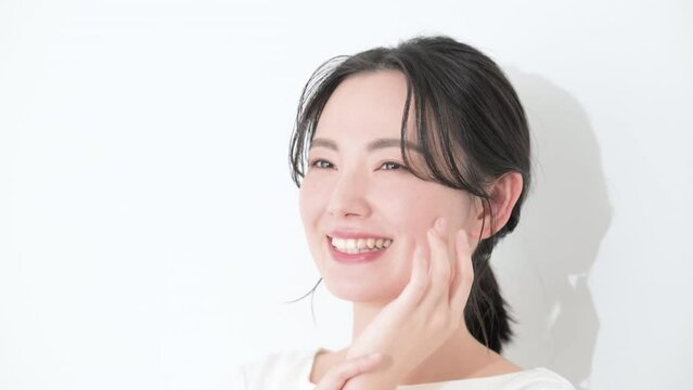 頬に手をあて笑顔のバストアップまとめ髪女性ビューティ　白背景のクローズアップの動画