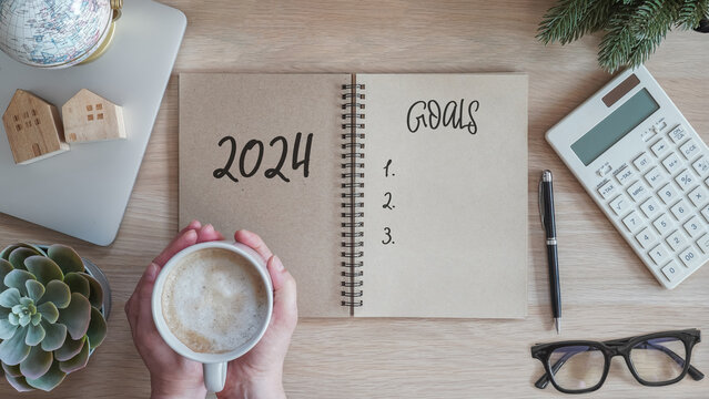 2024 goals new year resolutions on blank note book memo reminder wish list of yearly planner, action plan for work-life balance, good financial health, happy home family, travel aims on office desk