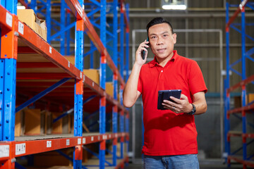 worker holding a tablet and talking on smartphone in the warehouse storage