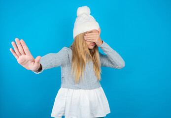 beautiful caucasian teen girl wearing grey sweater covers eyes with palm and doing stop gesture,...
