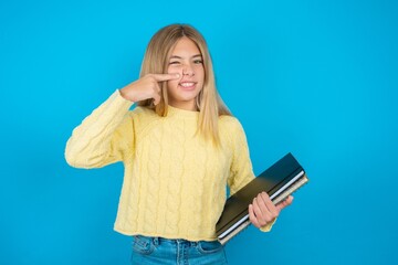 Naklejka premium beautiful caucasian teen girl wearing yellow sweater pointing unhappy to pimple on forehead, ugly infection of blackhead. Acne and skin problem