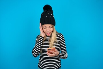 beautiful caucasian teen girl wearing striped sweater holding in hands cell reading sms using new...