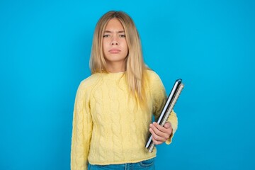 Offended dissatisfied beautiful caucasian teen girl wearing yellow sweater with moody displeased...