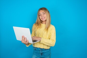 Adorable beautiful caucasian teen girl wearing yellow sweater holding modern device