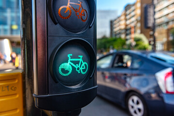 A green cycle lane traffic  signal at a junction in a busy London city street with a car passing in...