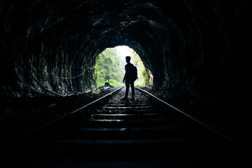 Silhouette of a man standing in a tunnel of rails. - obrazy, fototapety, plakaty