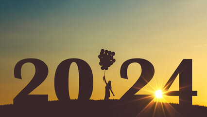 Happy girl holding balloons and standing in a field with numbers New Year 2024 at sunset. New Year and dreams