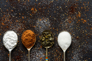 Spoons with icing sugar, green tea and cocoa on black background sprinkled with sugar, coffee,...