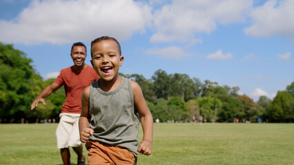 Father and son playing catch-up game outdoors running after each other through city park. Families....