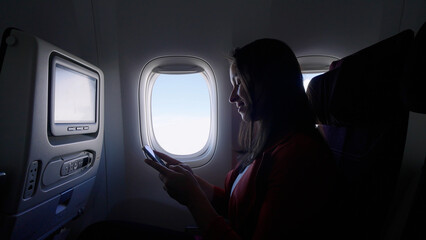 Caucasian female passenger chatting online via cellphone using wifi internet connection on board. Young woman browsing network during flight
 - obrazy, fototapety, plakaty