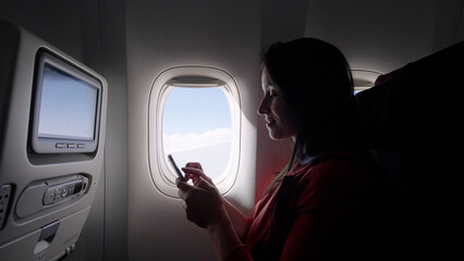 Caucasian female passenger chatting online via cellphone using wifi internet connection on board....