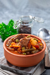 Beef stew with potato, green beans, carrot, peas and corn, in ceramic bowl, vertical, copy space