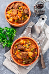Homemade beef stew with potato, green beans, carrot, peas and corn, in ceramic bowl, vertical, top
