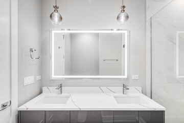 A modern, luxury bathroom with a white granite countertop, grey vanity cabinet, light fixtures...