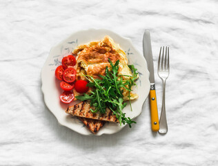 Cheese omelette, arugula, cherry tomatoes, whole grain toast - delicious breakfast on a light background, top view