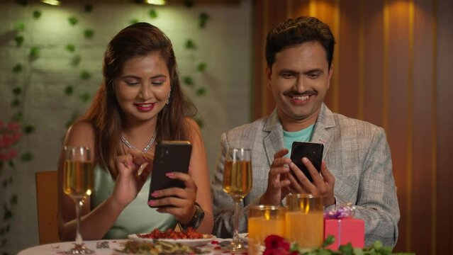 Indian couples at romantic candlelight dinner busy using mobile phone at restaurant - concept of social media sharing and technology distraction