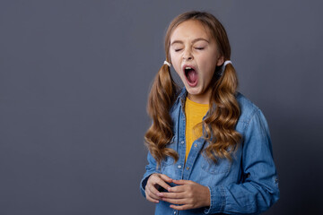 Teenage girl wants to sleep and yawns. Girl 10 years old in a denim shirt and a yellow blouse on a...