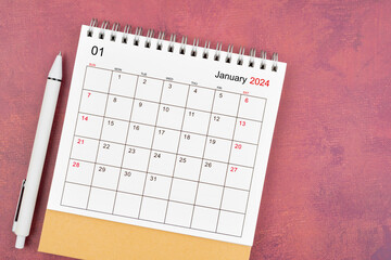 January 2024 desk calendar and pen on red background.