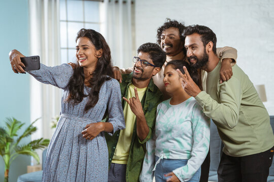 Group of friends taking selfie on mobile phone while gathering at home - concept of social media sharing, weekend holidays and carefree friendship.